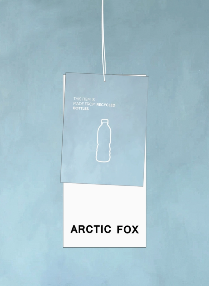 A hanging product tag for Arctic Fox, featuring a translucent light blue top section with a white bottle outline and the text 'THIS ITEM IS MADE FROM RECYCLED BOTTLES,' and a white bottom section with 'ARCTIC FOX' in black. The tag is suspended against a textured light blue background.